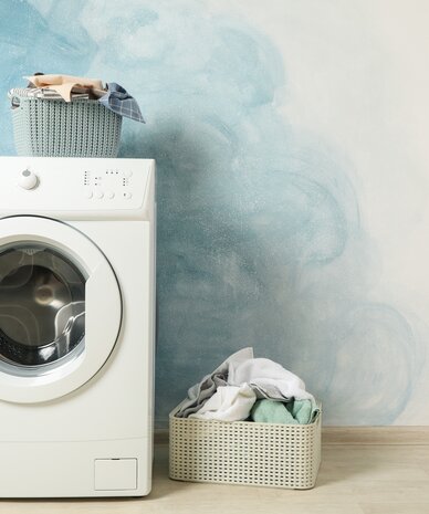White front-loading washing machine with a top laundry basket and clothes nearby