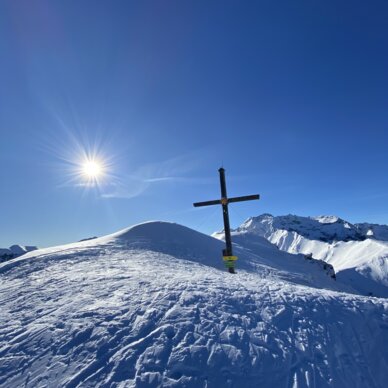 Snow-covered hill with wooden cross under blue sky