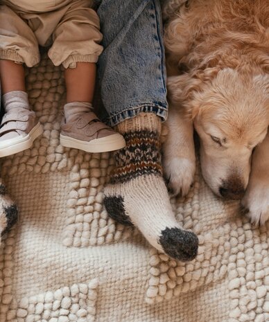 Kind sitzt neben schlummendem Hund auf Teppich | © prystai