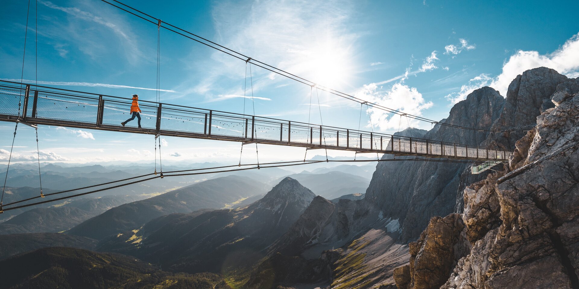 Schwebende Hängebrücke über felsiges Bergtal mit Wanderer