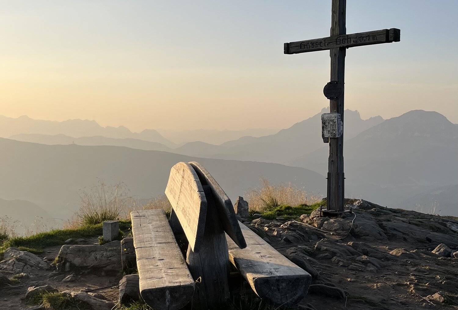 Holzbank und Schildpfosten auf felsigem Berggipfel bei Sonnenuntergang