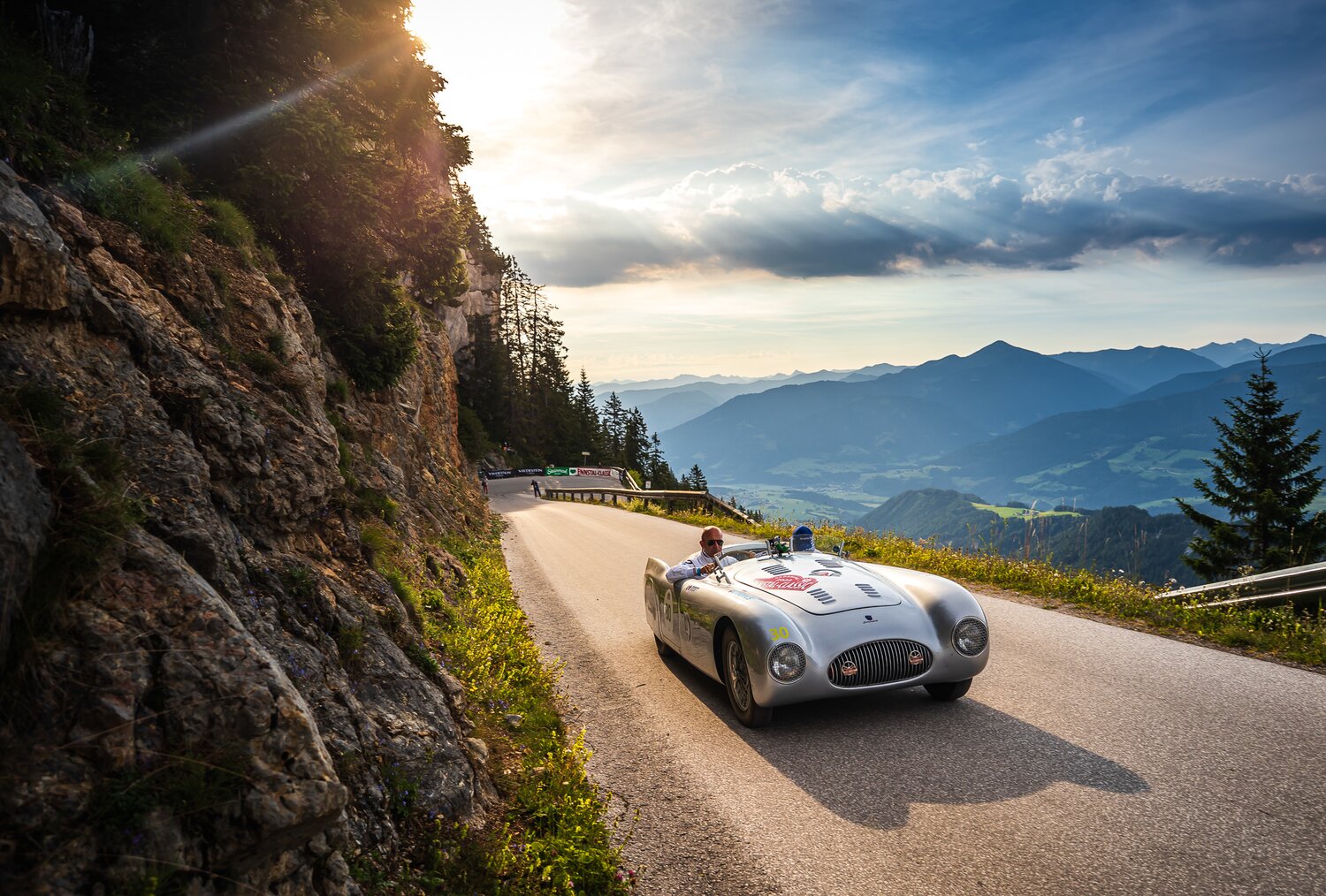 Silberner Oldtimer-Rennwagen fährt auf kurvenreicher Alpenstraße