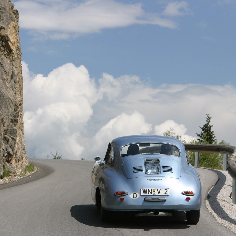 Blauer Vintage-Wagen fährt kurvenreicher Bergstraße am Felsvorsprung