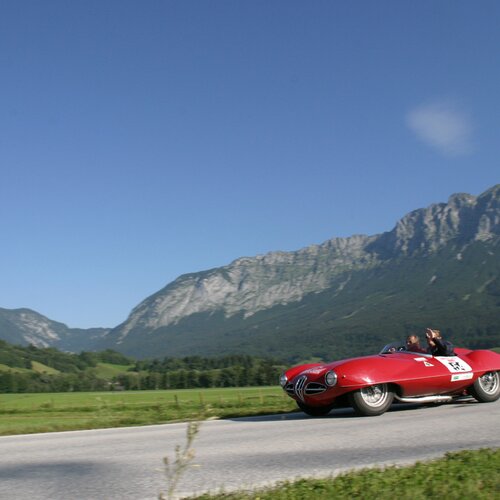 Roter Vintage-Rennwagen auf einer Landstraße vor Bergen