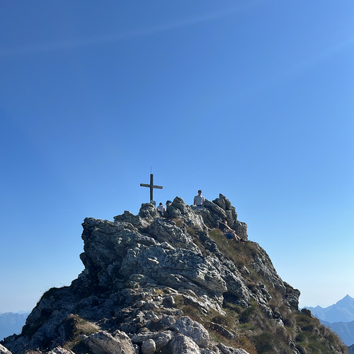 Felsiger Berggipfel mit Kreuz und Wanderern