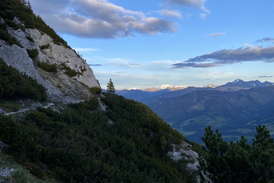 Felsiger Bergpfad mit grüner Vegetation und Wolken am Himmel