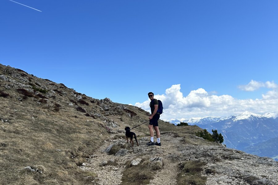 Wanderer mit Hund auf felsigem Bergpfad unter blauem Himmel