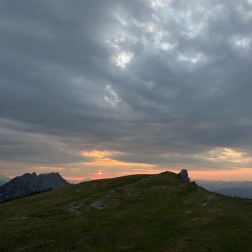 Grasiger Bergkamm mit Felsvorsprung bei Sonnenuntergang