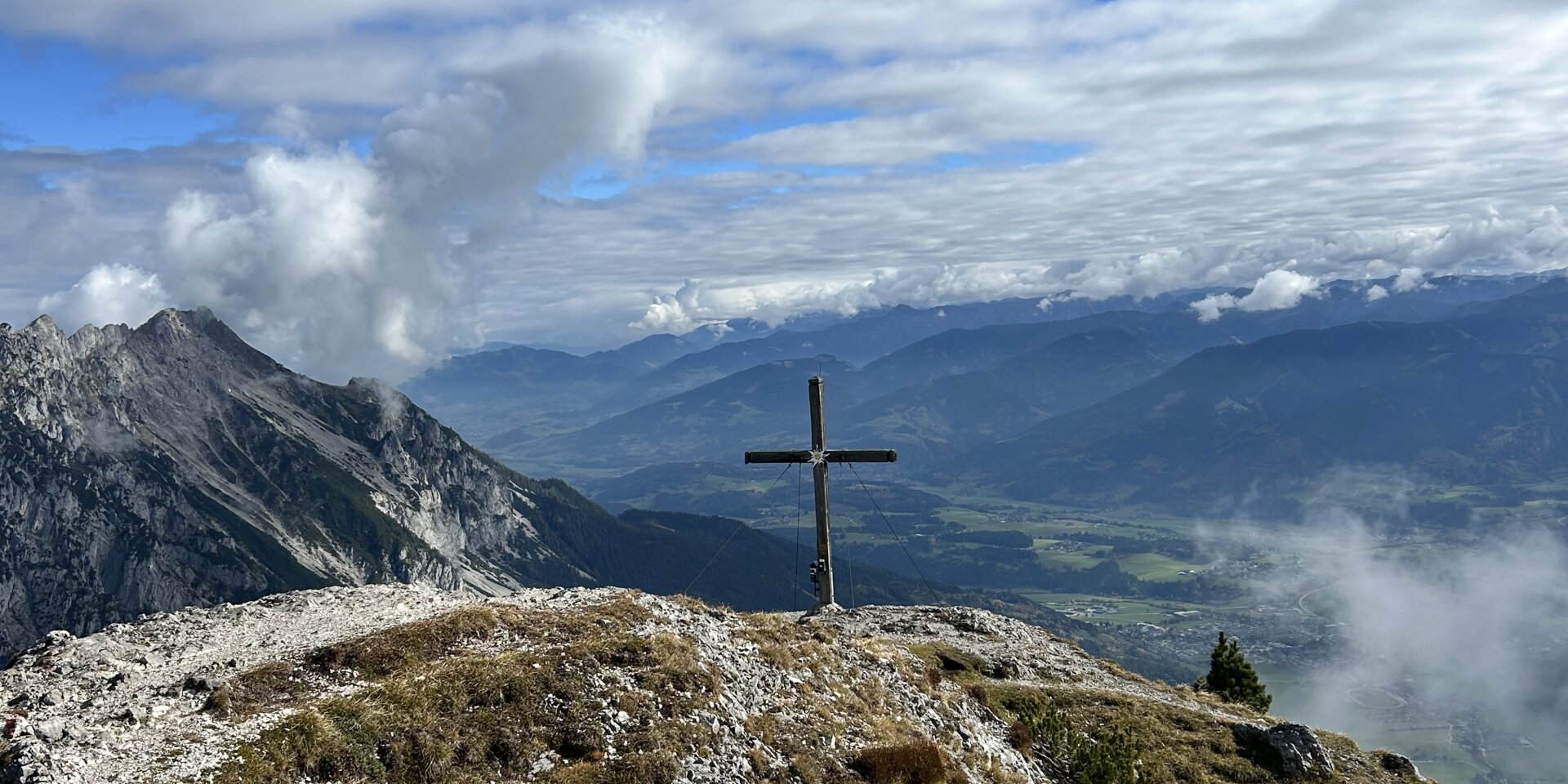 Holzkreuz auf felsigem Bergkamm vor Wolken