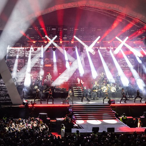 Outdoor concert stage with musicians performing, drums marked XXV, and bright spotlights. | © Harald Steiner