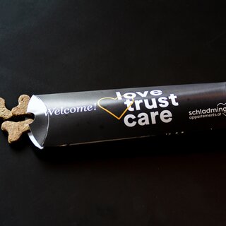 Gerolltes schwarzes Banner mit 'Willkommen!' und 'love trust care'-Text; Kekse daneben. | © SCHLADMING-APPARTEMENTS