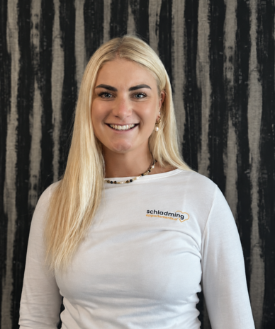 Lächelnde Frau in weißem Langarmshirt mit Schladming-Logo.