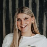 Lächelnde Frau mit langen blonden Haaren, weißes Shirt mit Logo schladming