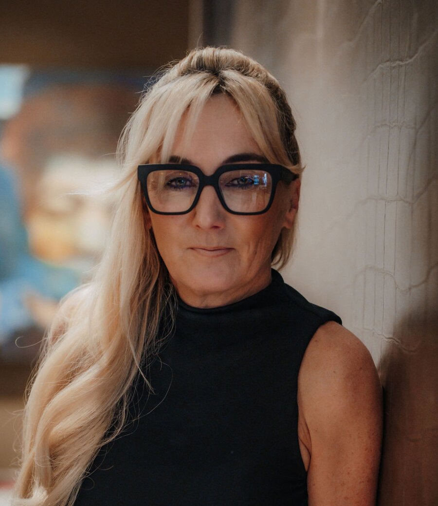 Frau mit langem blondem Haar, schwarzes ärmelloses Oberteil, große Brille