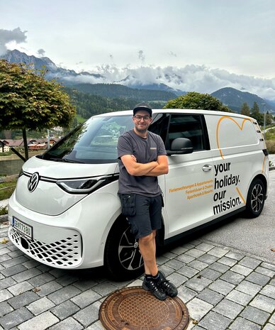 Mann vor weißem Van mit Berglandschaft im Hintergrund.