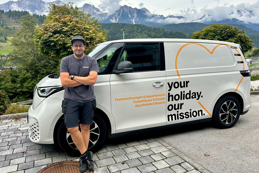 Mann lehnt an weißem Lieferwagen mit Slogan: your holiday. our mission