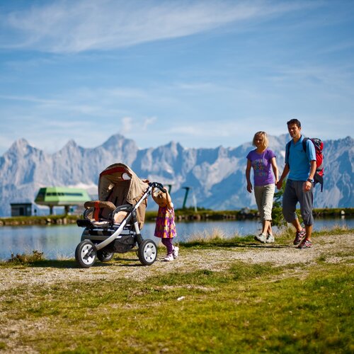 Familie mit Kinderwagen am See vor Bergen