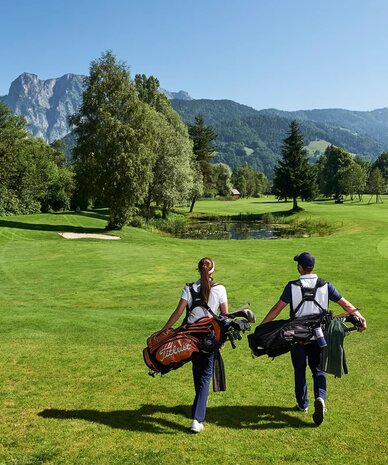 Zwei Golfer gehen über den sonnigen Golfplatz mit Bergkulisse