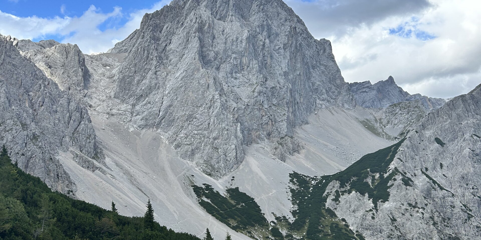 Wuchtiger Felsgipfel vor grünem Wald und blauem Himmel