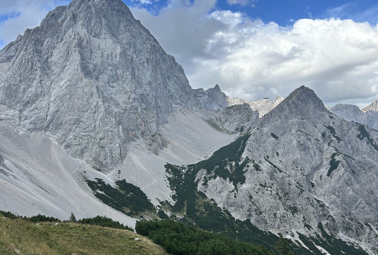 Imposanter grauer Berggipfel mit felsigen Hängen und grünem Vordergrund.