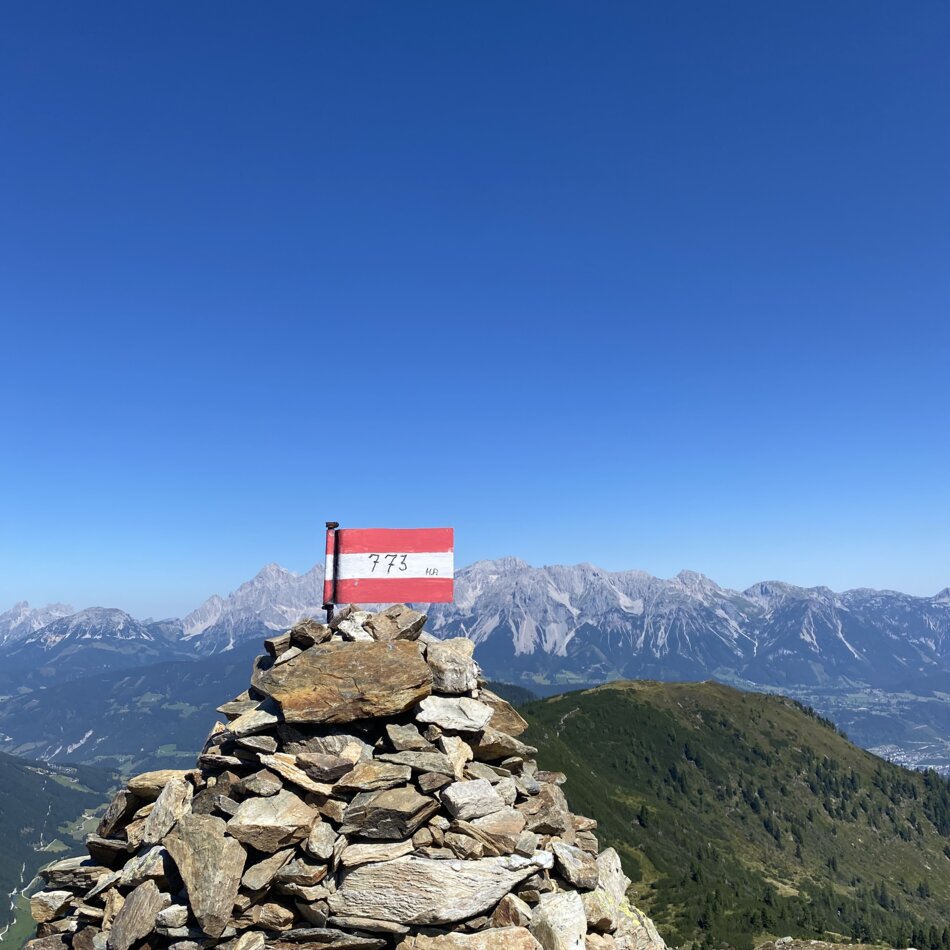 Rock cairn with red-white marker sign reading 773, mountains behind