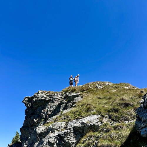 Two hikers stand atop a rocky cliff under blue sky