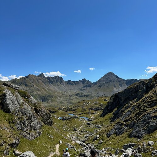 Hikers walking along a rocky mountain trail under blue sky.