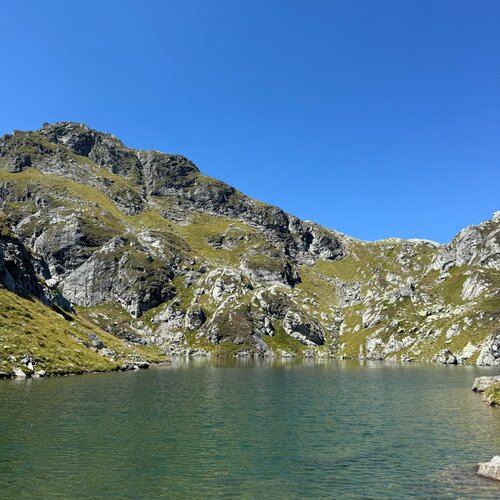 Rocky mountain slope with grassy patches beside a lake