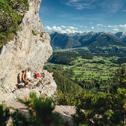 Zwei Wanderer sitzen auf steinigem Felsvorsprung mit Ausblick