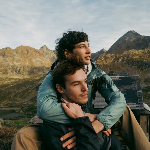 Zwei Wanderer umarmen sich auf einer Veranda mit Blick auf Berge.
