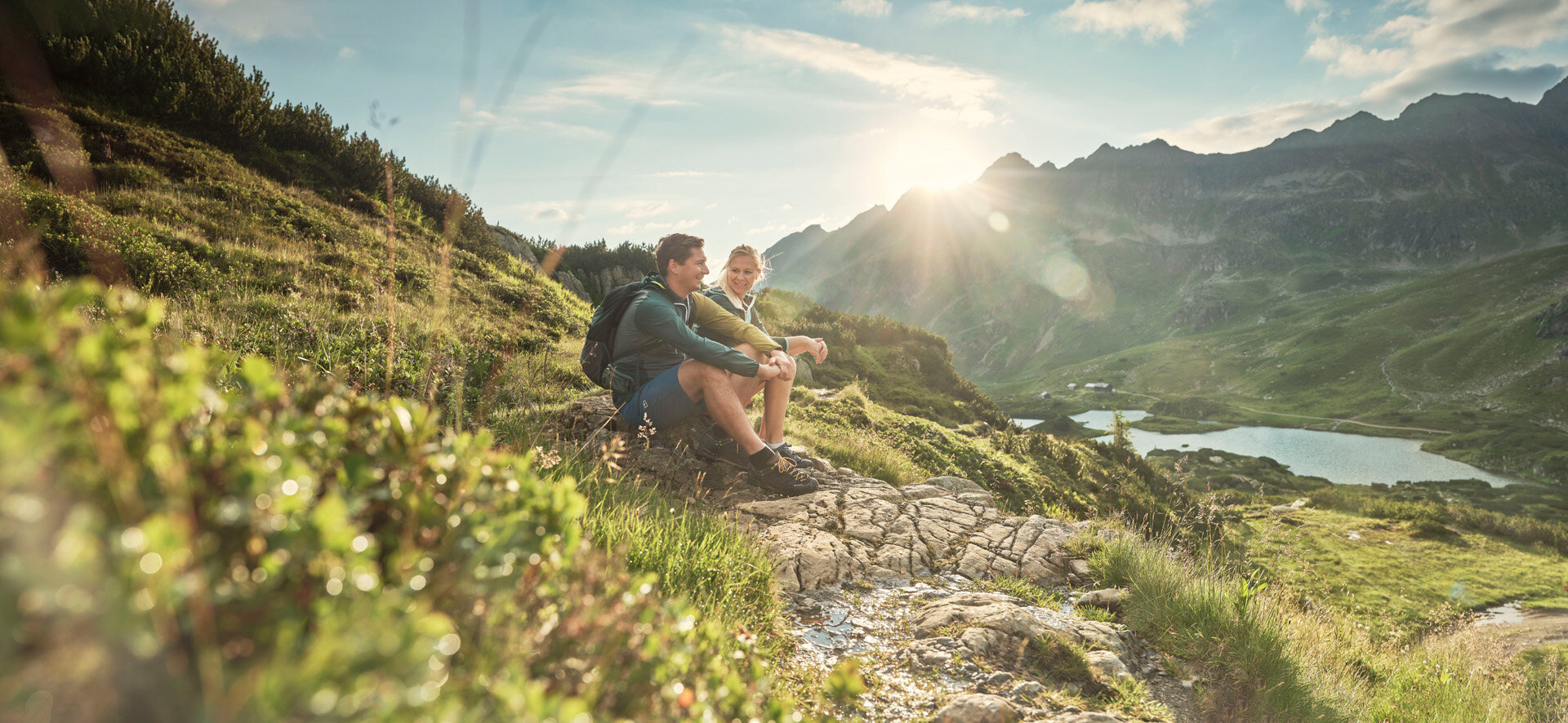 Zwei Wanderer ruhen auf felsiger Steigung mit Alpenblick