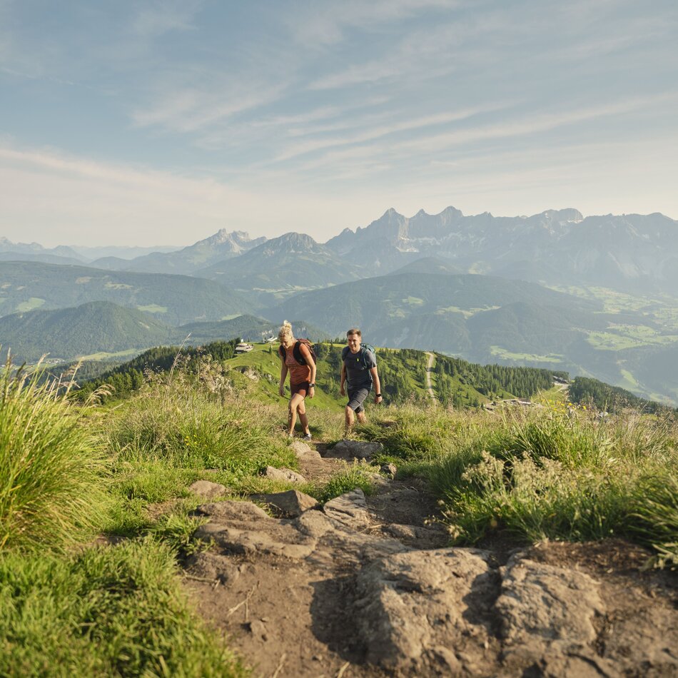 Zwei Wanderer wandern einen felsigen Bergpfad mit Tal und Gipfeln