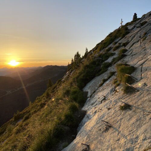 Sonnenuntergang über bergiger Landschaft mit Felswand und Metallstufen