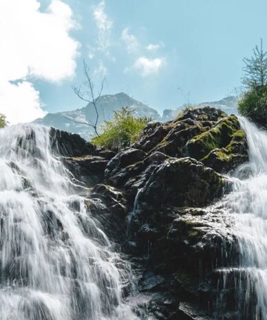 Wasserfall über Felsen, umgeben von grüner Vegetation und blauem Himmel