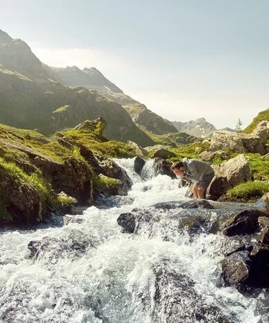 Zwei Wanderer neben einem rauschenden Gebirgsbach in alpiner Landschaft