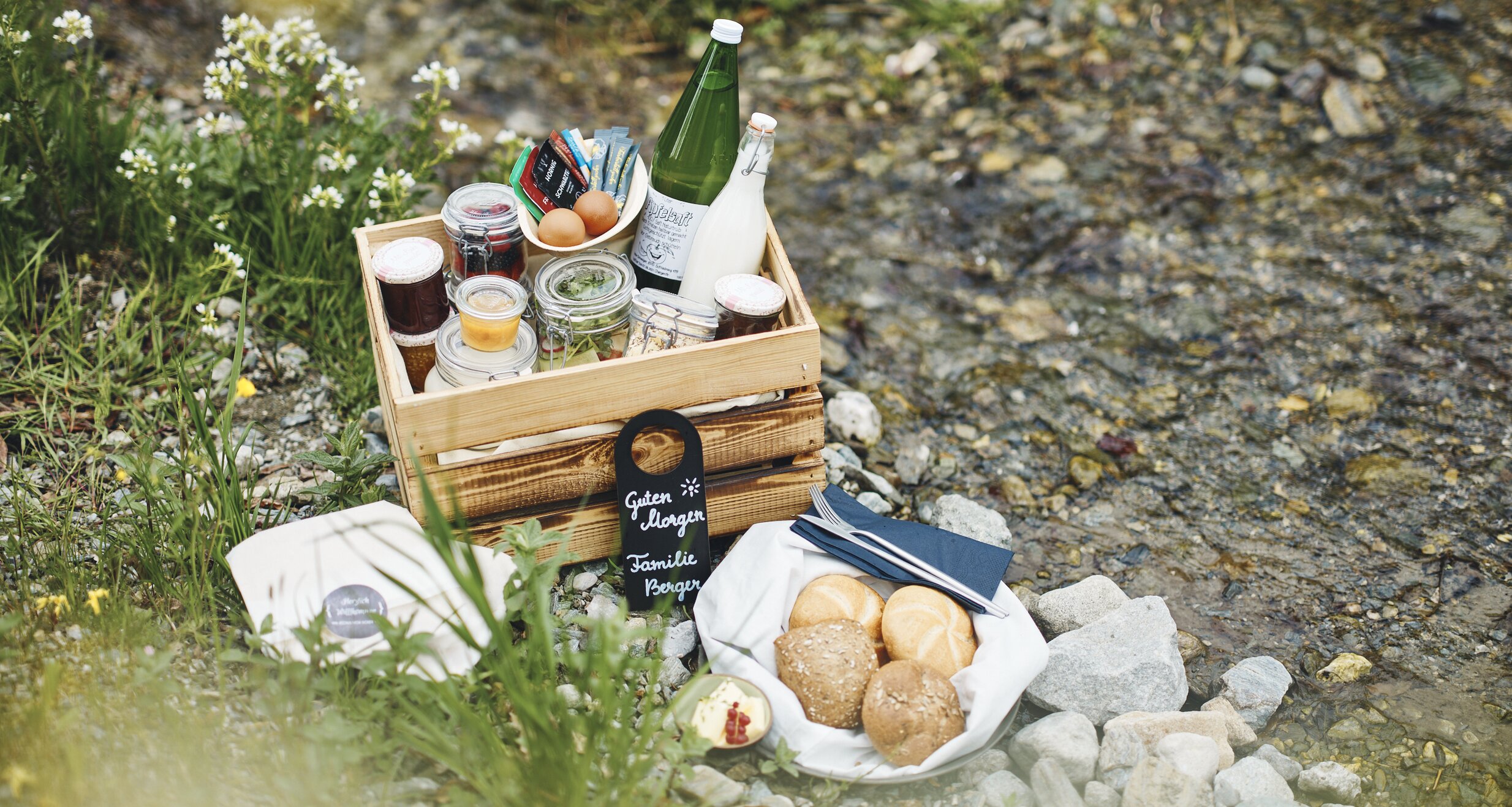 Picnic setup beside a rocky stream with jars and bread. | © RAPHAELGABAUER.COM
