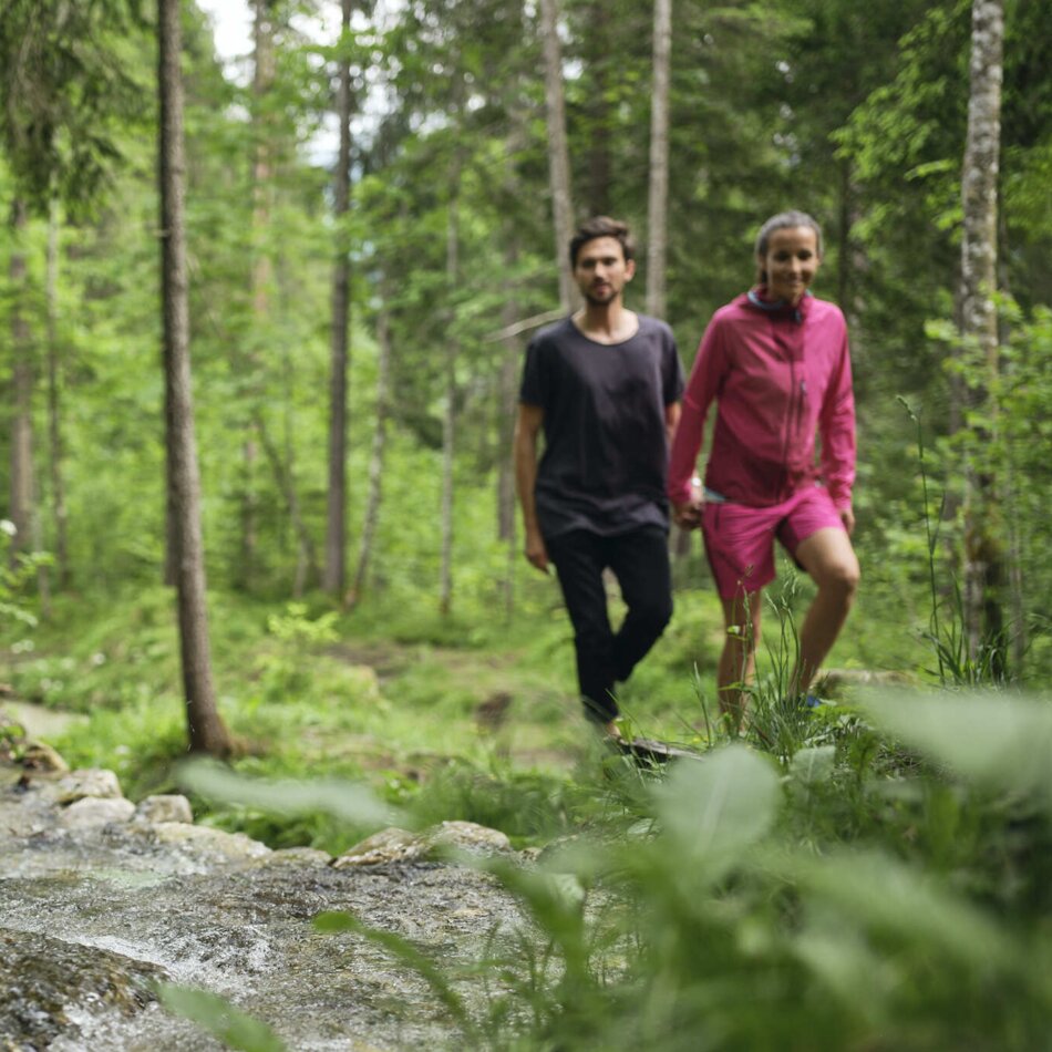Mädchen am Waldbach, zwei Personen im Hintergrund | © RAPHAELGABAUER.COM