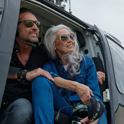 Zwei Erwachsene im geöffneten Helikopter, tragen Sonnenbrillen.