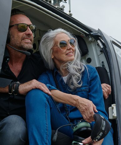 Zwei Erwachsene im geöffneten Helikopter, tragen Sonnenbrillen.