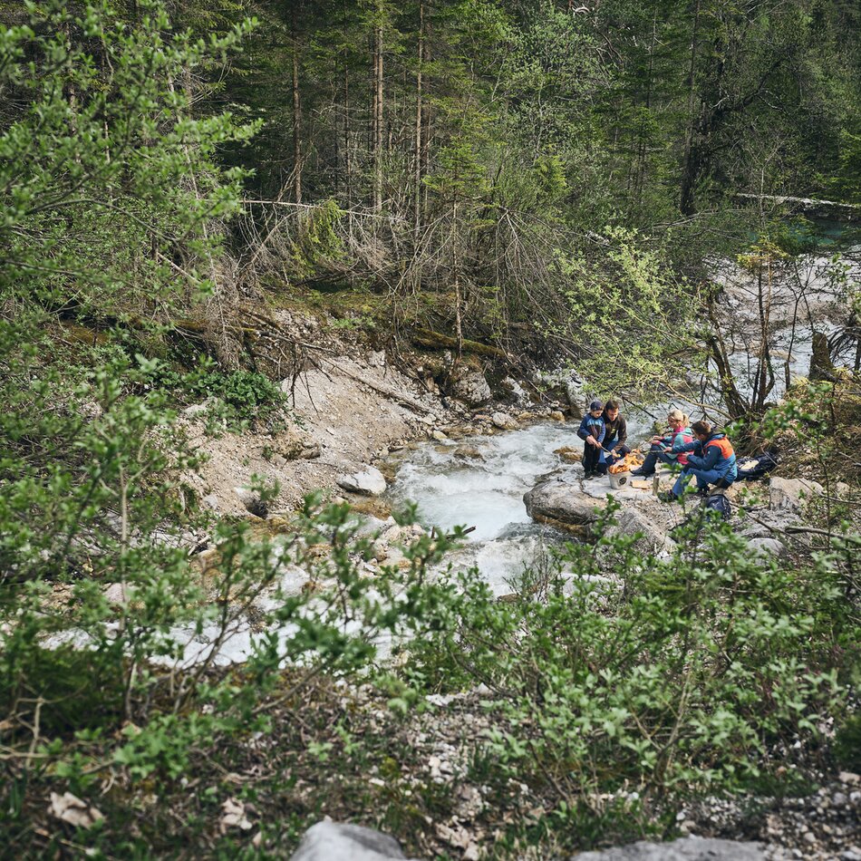Gruppe Wanderer sitzt auf Felsen neben Waldbach | © RAPHAELGABAUER.COM