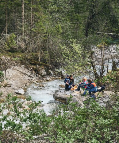 Gruppe Wanderer sitzt auf Felsen neben Waldbach | © RAPHAELGABAUER.COM