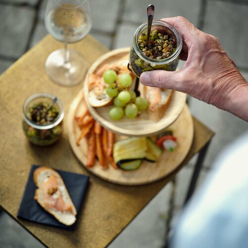 Hand hält Glas mit Oliven über Käseplatte | © RaphaelGabauer