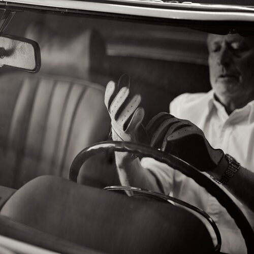 Älterer Mann trägt Fahrhandschuhe im Innenraum eines Oldtimers. | © RaphaelGabauer