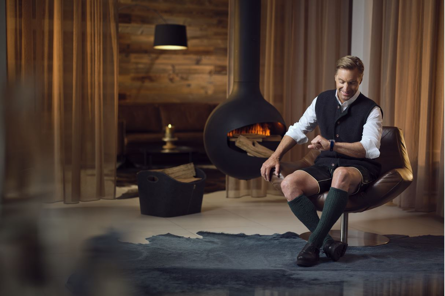 Mann sitzt im gemütlichen Wohnzimmer am Kamin und schaut auf die Uhr | © Katharina Knapp