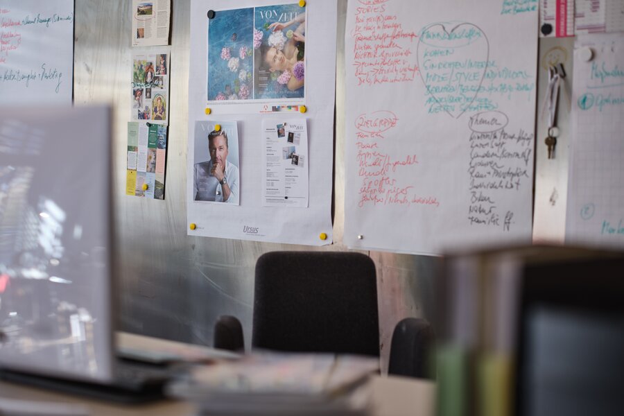 Bürowand mit Postern, Notizen und Stuhl davor | © RAPHAELGABAUER.COM