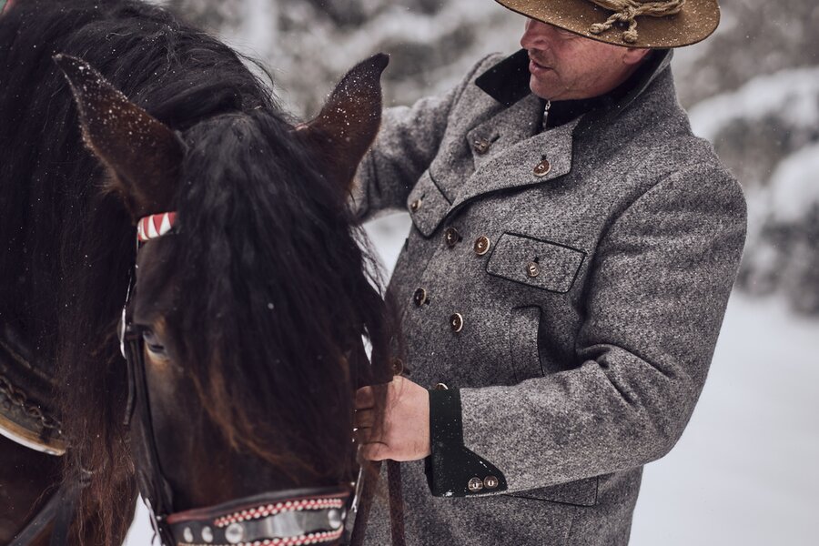 Mann in grauem Wollmantel führt ein Pferd im Schnee | © RAPHAELGABAUER.COM