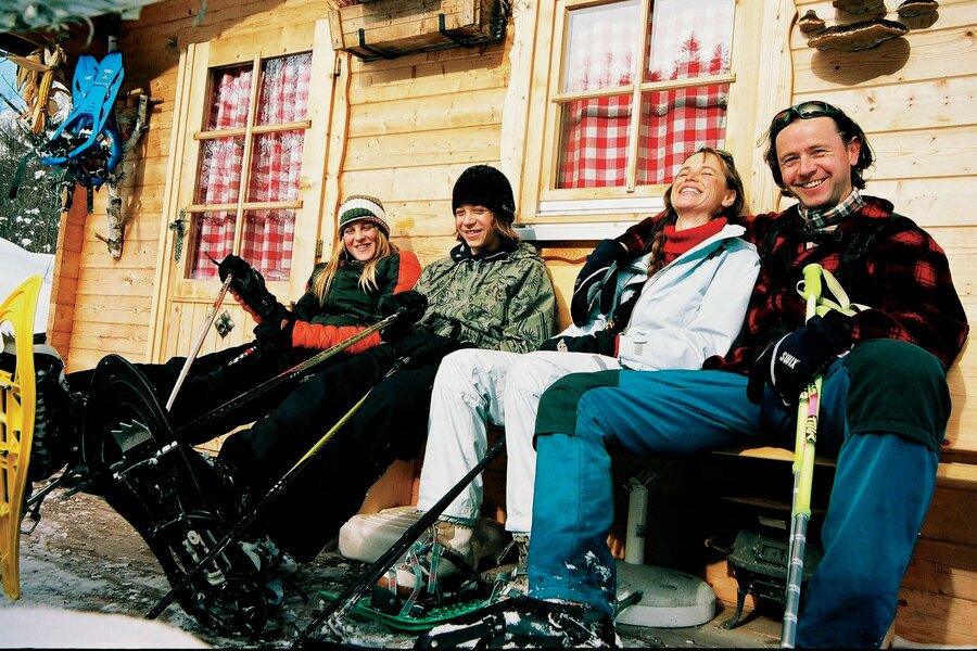 Gruppe von Freunden in Winterkleidung sitzt vor Holzhütte.