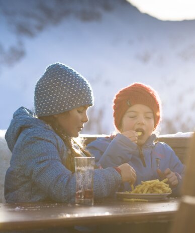 Zwei Kinder in Winterjacken essen Pommes im Freien. | © Claudia Ziegler