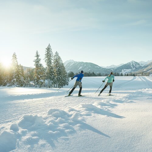 Zwei Skifahrer gleiten durch eine schneebedeckte Winterlandschaft. | © Peter Burgstaller