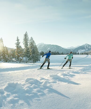 Zwei Skifahrer gleiten durch eine schneebedeckte Winterlandschaft. | © Peter Burgstaller
